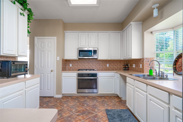 kitchen featuring tasteful backsplash, white cabinetry, stainless steel appliances, sink, and dark tile floors