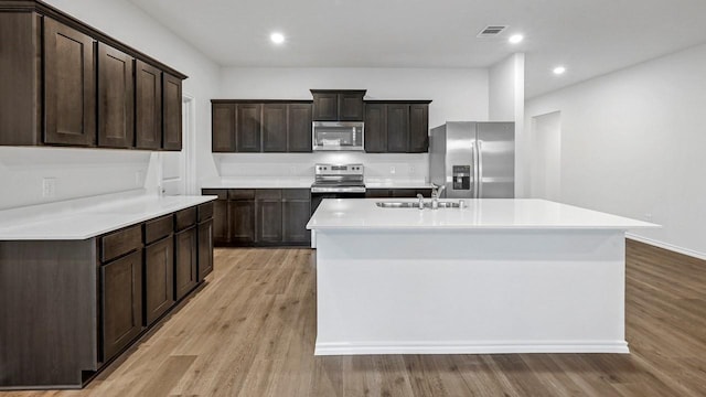 kitchen with dark brown cabinetry, light wood-type flooring, stainless steel appliances, and sink