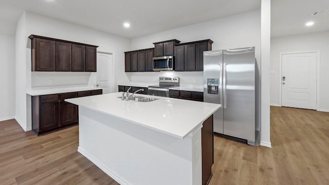 kitchen with a kitchen island with sink, stainless steel appliances, dark brown cabinetry, light hardwood / wood-style floors, and sink