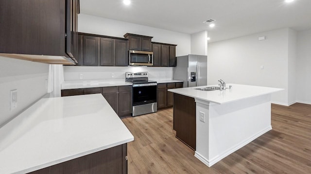 kitchen with an island with sink, appliances with stainless steel finishes, sink, and light wood-type flooring