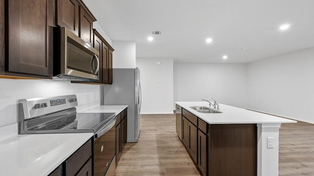 kitchen with a center island with sink, stainless steel appliances, dark brown cabinetry, light hardwood / wood-style flooring, and sink