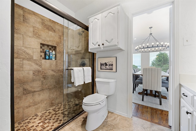 bathroom with tile flooring, an inviting chandelier, a shower with shower door, vanity, and toilet