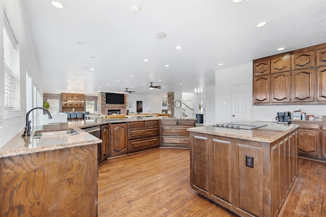 kitchen with light stone countertops, a fireplace, light wood-type flooring, sink, and ceiling fan