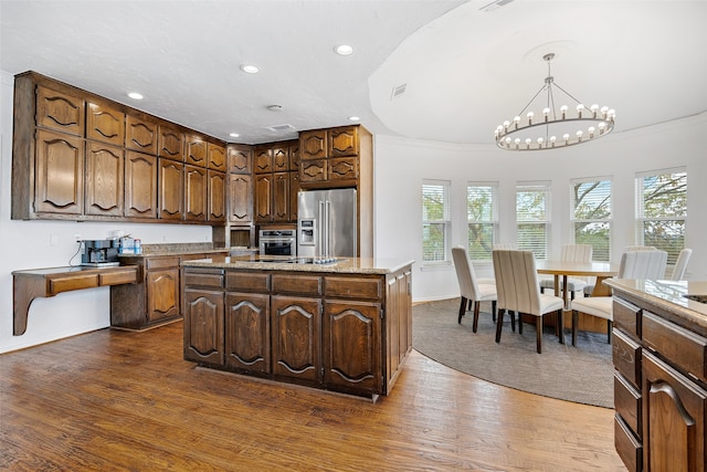 kitchen with stainless steel appliances, a kitchen island with sink, wood-type flooring, pendant lighting, and a chandelier