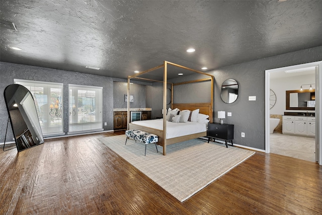 bedroom featuring wood-type flooring, connected bathroom, and a textured ceiling