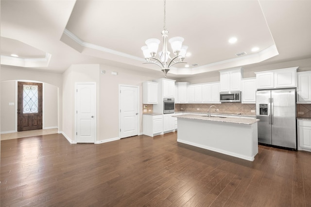 kitchen featuring a kitchen island with sink, hanging light fixtures, stainless steel appliances, white cabinets, and a raised ceiling