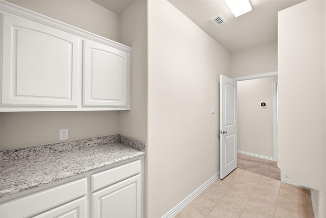 interior space featuring light tile patterned flooring, white cabinets, and light stone counters