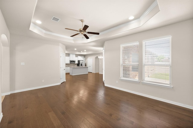 unfurnished living room with dark hardwood / wood-style floors, ceiling fan, ornamental molding, and a tray ceiling