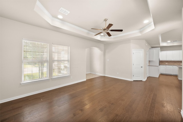 unfurnished living room featuring dark wood-type flooring, ceiling fan, crown molding, and a raised ceiling