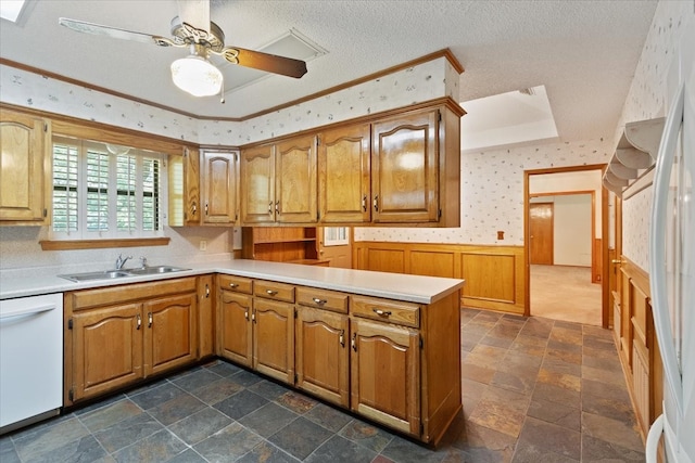 kitchen featuring a wainscoted wall, a sink, white appliances, a peninsula, and wallpapered walls