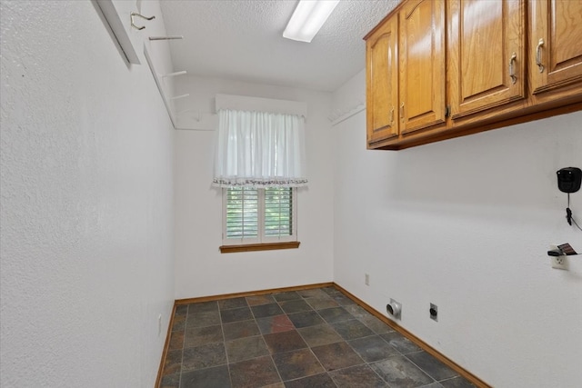 laundry area featuring cabinet space, a textured ceiling, stone finish flooring, and baseboards