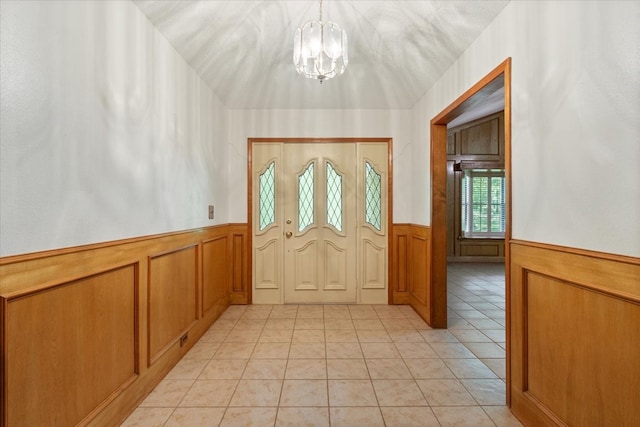 foyer featuring a notable chandelier, light tile patterned flooring, and a wainscoted wall