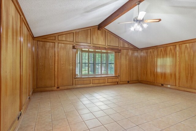 spare room with light tile patterned floors, vaulted ceiling with beams, ceiling fan, wood walls, and a textured ceiling