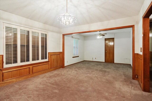 carpeted empty room with a wainscoted wall, a textured ceiling, and ceiling fan with notable chandelier