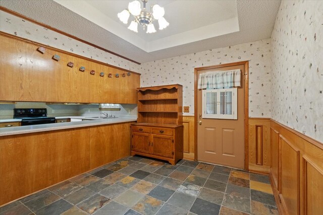 kitchen with wallpapered walls, a raised ceiling, black electric range oven, and wainscoting