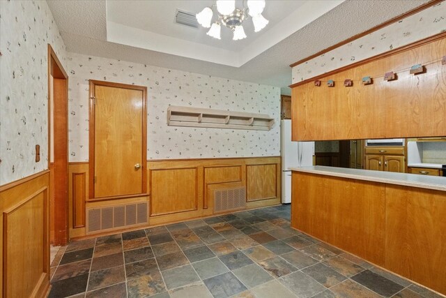 kitchen featuring wallpapered walls, a tray ceiling, wainscoting, brown cabinets, and freestanding refrigerator