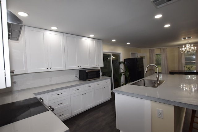 kitchen with dark wood-type flooring, black fridge, a notable chandelier, sink, and white cabinetry