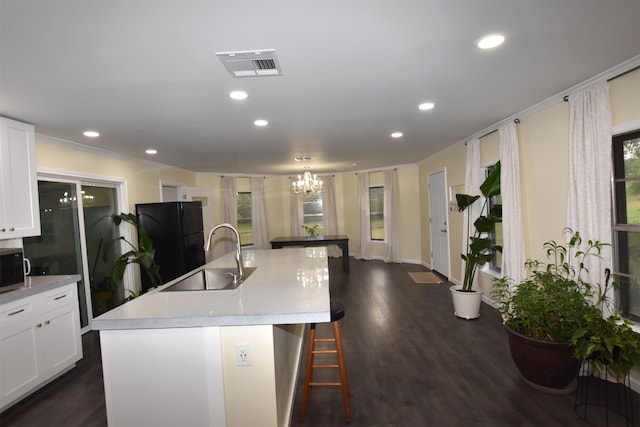 kitchen featuring an island with sink, sink, black refrigerator, and dark wood-type flooring