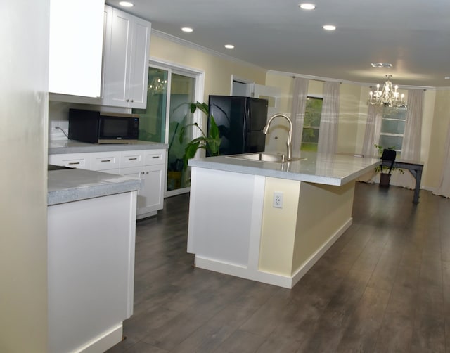 kitchen with dark hardwood / wood-style flooring, black fridge, a kitchen island with sink, white cabinets, and sink