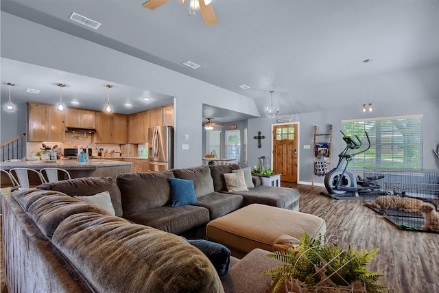 living room featuring a fireplace, ceiling fan with notable chandelier, dark hardwood / wood-style floors, and vaulted ceiling