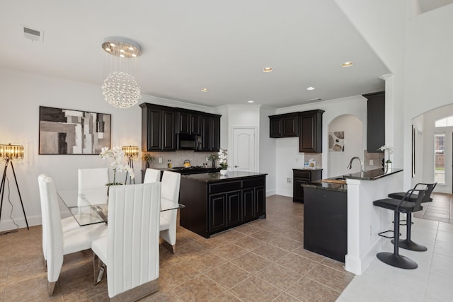 kitchen with dark stone countertops, an inviting chandelier, a kitchen breakfast bar, light tile patterned floors, and backsplash