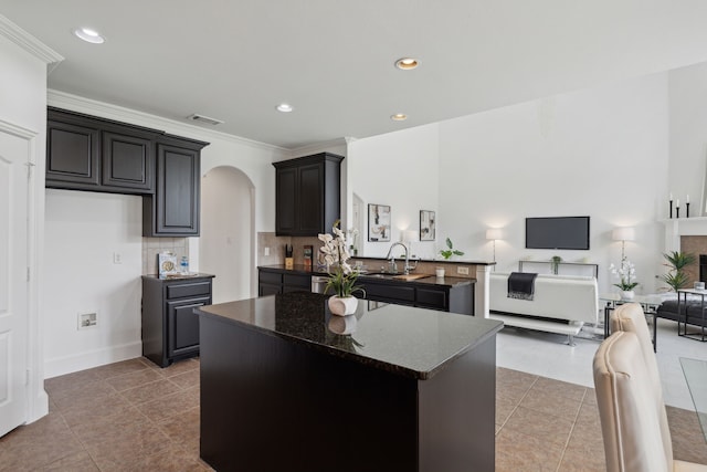 kitchen featuring dark stone counters, light tile patterned flooring, tasteful backsplash, sink, and a center island