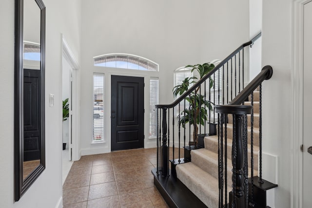 tiled entryway featuring stairway, a towering ceiling, and baseboards