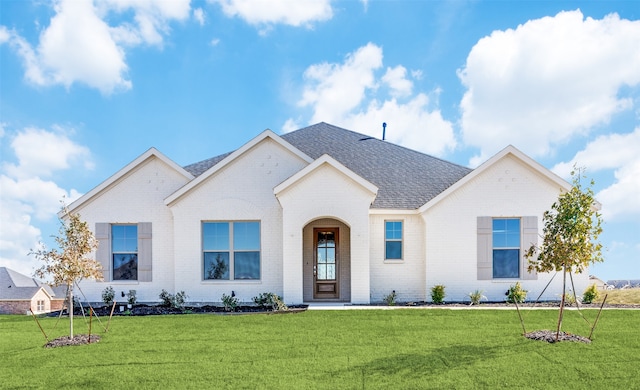 view of front of property with a shingled roof, a front yard, and brick siding