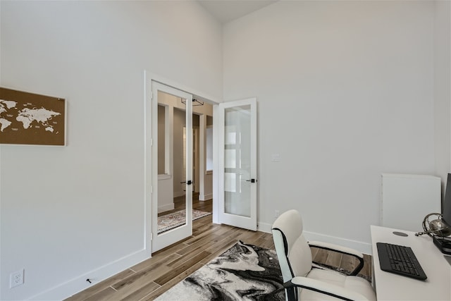 home office with a towering ceiling, french doors, and hardwood / wood-style floors