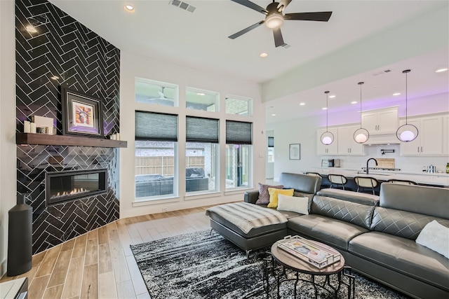 living room with ceiling fan, a tiled fireplace, light wood-type flooring, and sink