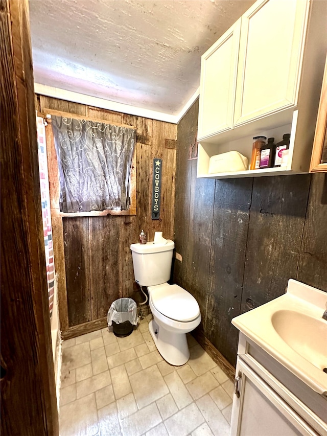 bathroom with vanity, wood walls, and toilet