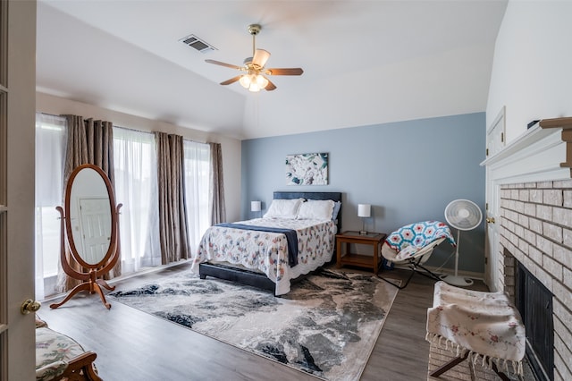 bedroom with wood-type flooring, a brick fireplace, vaulted ceiling, and ceiling fan