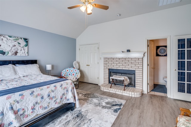 bedroom with a fireplace, lofted ceiling, connected bathroom, hardwood / wood-style floors, and ceiling fan