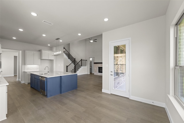 kitchen featuring light wood-type flooring, a stone fireplace, hanging light fixtures, blue cabinets, and white cabinetry