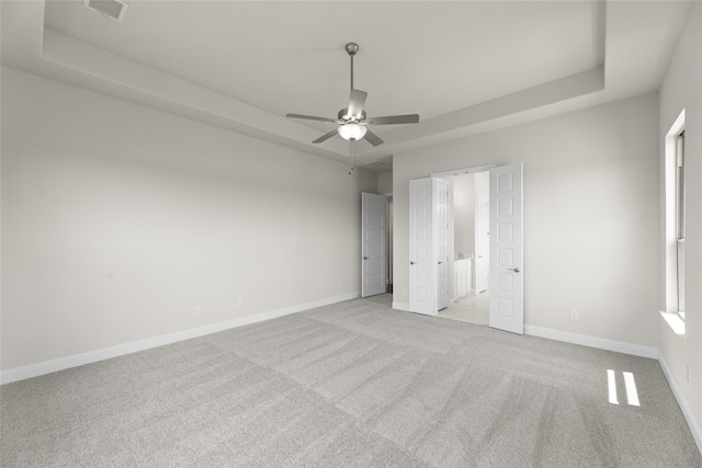 unfurnished bedroom featuring ceiling fan, a raised ceiling, and light carpet