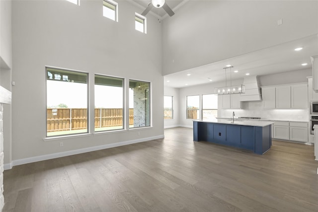 unfurnished living room with a towering ceiling, ceiling fan, and wood-type flooring