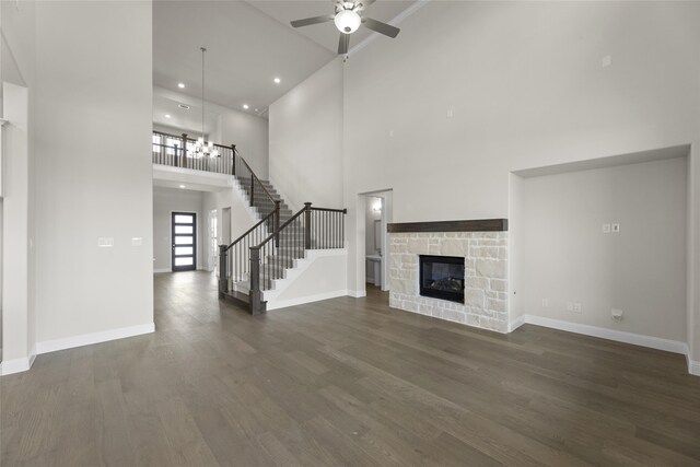 unfurnished living room featuring a high ceiling, ceiling fan, dark wood-type flooring, and a stone fireplace