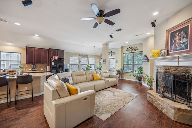 living room featuring a stone fireplace, dark hardwood / wood-style floors, and ceiling fan