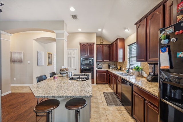 kitchen with a kitchen island, backsplash, black appliances, a breakfast bar, and lofted ceiling