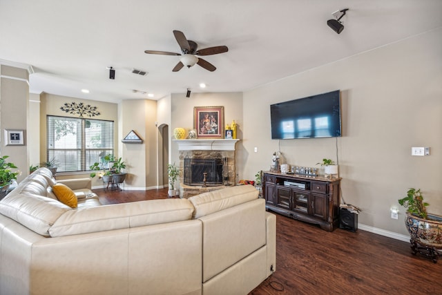 living room with a stone fireplace, ceiling fan, and dark wood-type flooring