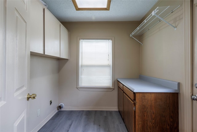 clothes washing area featuring light wood-type flooring, cabinet space, baseboards, and a textured ceiling