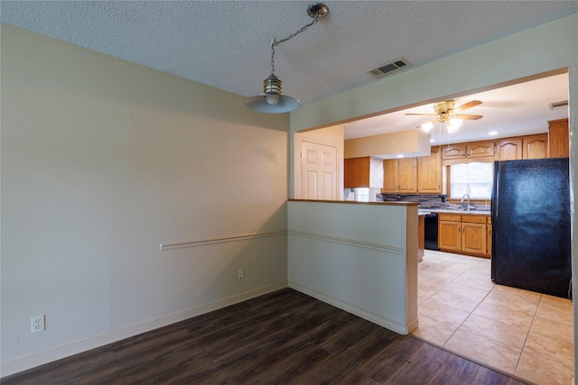 kitchen with visible vents, baseboards, light wood-style floors, black appliances, and brown cabinetry