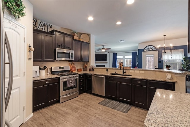 kitchen with light hardwood / wood-style floors, kitchen peninsula, ceiling fan with notable chandelier, sink, and appliances with stainless steel finishes