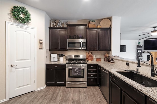 kitchen with sink, light stone counters, light wood-type flooring, and appliances with stainless steel finishes