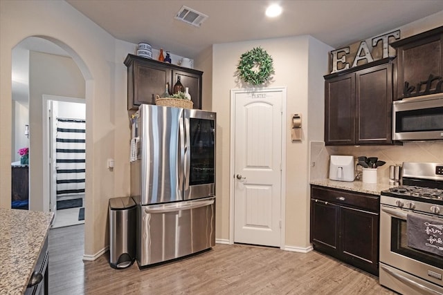 kitchen with tasteful backsplash, light wood-type flooring, dark brown cabinetry, light stone counters, and appliances with stainless steel finishes