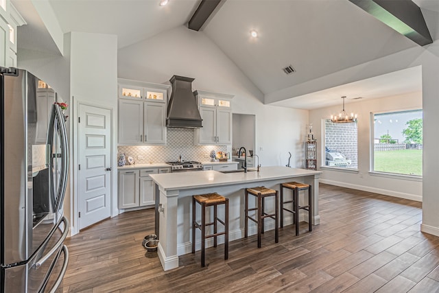 kitchen featuring custom exhaust hood, an island with sink, stainless steel appliances, beamed ceiling, and hanging light fixtures