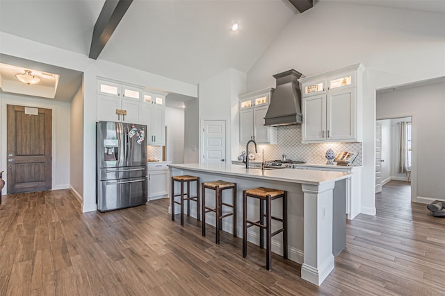 kitchen featuring beam ceiling, premium range hood, stainless steel fridge with ice dispenser, and a center island with sink