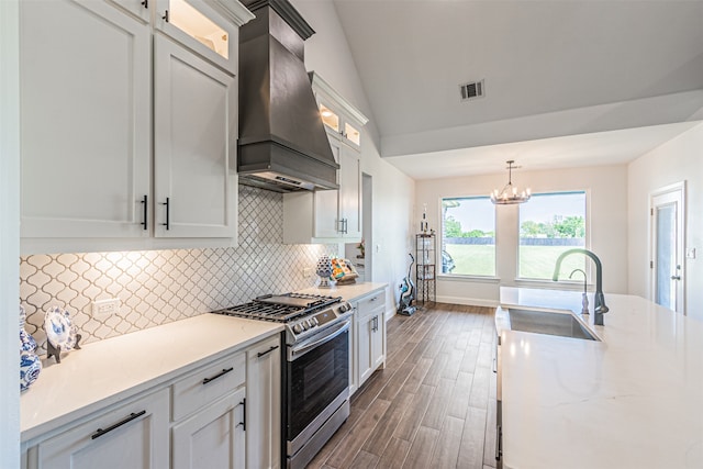 kitchen with decorative light fixtures, vaulted ceiling, custom exhaust hood, stainless steel range with gas cooktop, and white cabinets