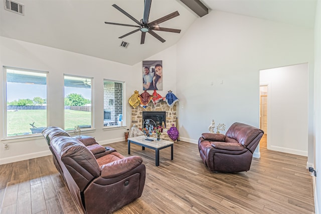 living room featuring a stone fireplace, ceiling fan, beam ceiling, high vaulted ceiling, and hardwood / wood-style flooring