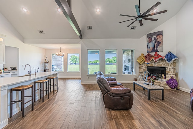 living room featuring a stone fireplace, beam ceiling, ceiling fan with notable chandelier, dark hardwood / wood-style flooring, and sink